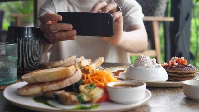 Close of human hands taking pictures of food served on a wooden table. Vegan breakfast as content for food blog