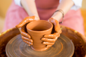 Fototapeta na wymiar Woman hands sculpts cup from clay pot. Workshop of modeling on potter wheel.