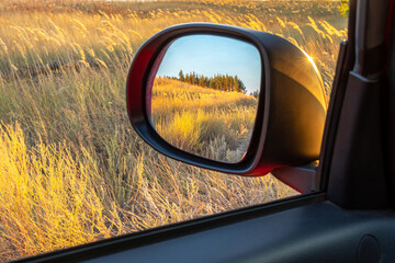Reflected field and forest in rearview mirror at sunset. Concept of car eco travel around your country, travel to future or past, ways to change