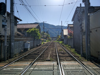 Obraz premium KYOTO, JAPAN - APRIL 5, 2018: Railroad tracks in the city of Arashiyama, Kyoto. The railway goes into the distance to the station, along the tracks there are houses with cherry blossoms.