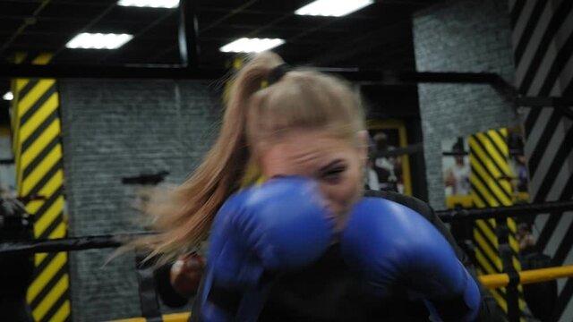 Portrait of a young focused woman during boxing training, she practices punches in front of the camera.