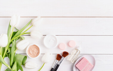 Top view of cosmetic creams and soap with white tulips top view flat lay on white wooden background