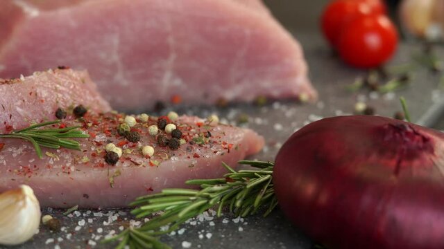 Close up of fresh pork is sprinkled with peppercorns, spices and seasonings on background of onion, garlic and greens. Food concept, cooking meat, loin, carbonate.