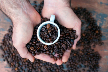 grãos de café em uma xícara nas mãos masculinas. 
