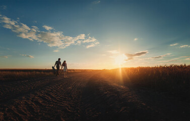 Fototapeta na wymiar A young newlyweds couple in love is walking holding hands to meet the sunset.Silhouette of a guy with a guitar who leads his girlfriend along road between wheat fields.Country style.View from the back