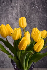 bouquet of yellow tulips in a vase on a gray background 
