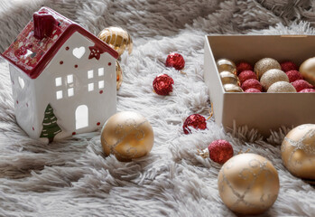 Christmas decorations on the background of a light plaid. A box with Christmas balls , a house with a red roof.