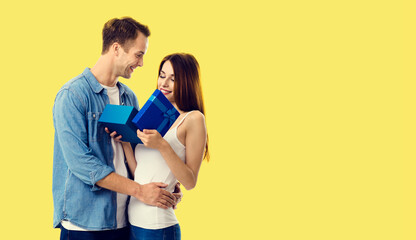 Love, dating, celebrating, lovers concept - happy smiling amorous couple opening gift box. Studio portrait of young man and woman, isolated over yellow background.