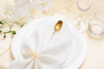 Beautiful festive table setting with white napkin and white orchids and golden cutlery on light background