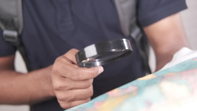 young man using magnifying glass looking something on map 