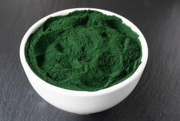 Spirulina powder in a white bowl on a black background. Healthy food concept. Horizontal orientation. Close-up.