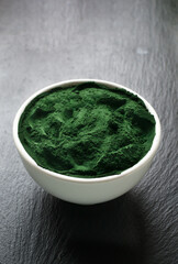 Spirulina powder in a white bowl on a stone background. Healthy food concept. Vertical orientation. Copy space.