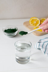 A glass of water and a teaspoon of spirulina in your home kitchen. Healthy food concept. Vertical orientation. Copy space.