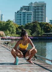 Tired sportswoman with bottle crouching at park and looking away.
Attractive asian female runner in...