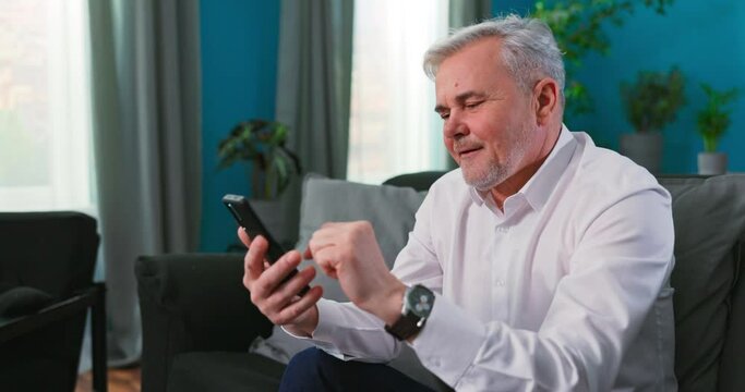 Smiling senior old man talking using cell phone computer modern tech at home on weekend lifestyle, happy elderly grandfather doing internet shopping choose sale offers