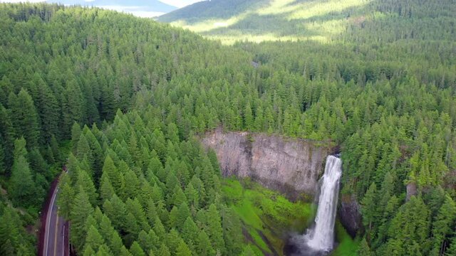 Aerial panning shot of highway near beautiful waterfall amidst trees, drone flying near cascade in forest - Salt Creek Falls, Oregon
