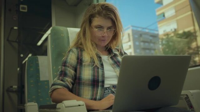 Young woman on commuter train to city or airport express work remotely on laptop, send emails, reply to texts from laptop connected to internet hotspot.Millennial freelancer commute and stay connected