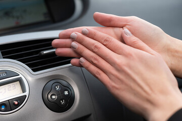 The woman warms her hands over the car's hot air outlet. Cold hands.
