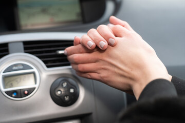 The girl squeezes her hands and warms them over the hot air outlet in the car. Cold hands.