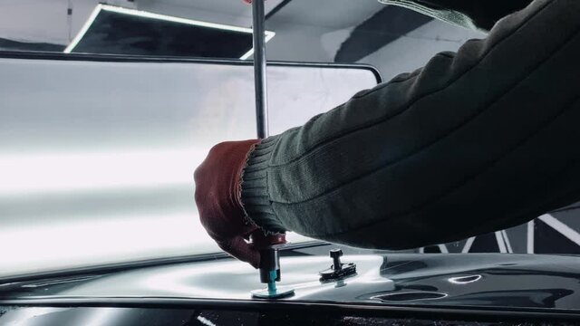 Car mechanic in car service with tools for repairing dents in car body.