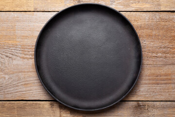 Empty cast iron frying pan on wooden culinary background. Space for text.