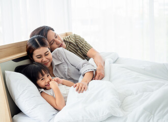 happy family having fun in bed room concept. father,mother and daugther smiling face, kiss love together lying on bed with duvet cover them copy space.