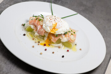 Poached egg on a bed of leek and marinated fresh salmon, chive sauce, on white plate