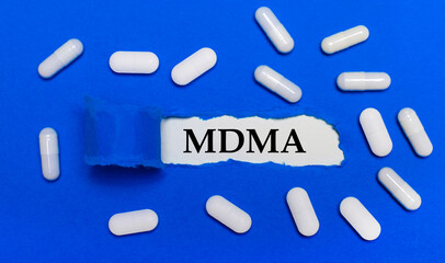 White pills lie on a beautiful blue background. In the center is white paper with the inscription MDMA. Medical concept. View from above.
