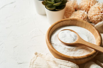 beauty concept of collagen powder in a wooden bowl and spoon on white table background. health supplement, protein intake. flower and green plant