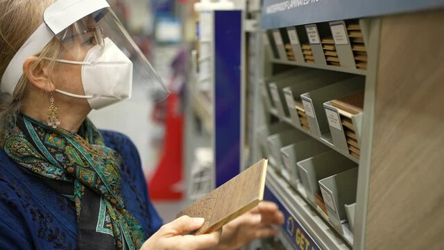 Mature woman wearing face shield and mask looking at wood flooring materials in a big box hardware store.