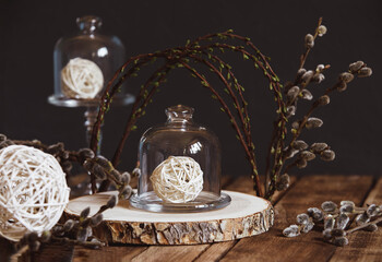 Easter spring composition of spring willow branches in the form of an arch, rattan white balls in a glass bowl cloche. The concept of rustic Easter and wedding decoration. Selective soft focus.
