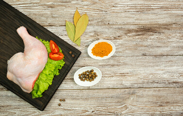 Raw chicken legs on green lettuce leaves, allspice, turmeric, bay leaf on a brown wooden background.