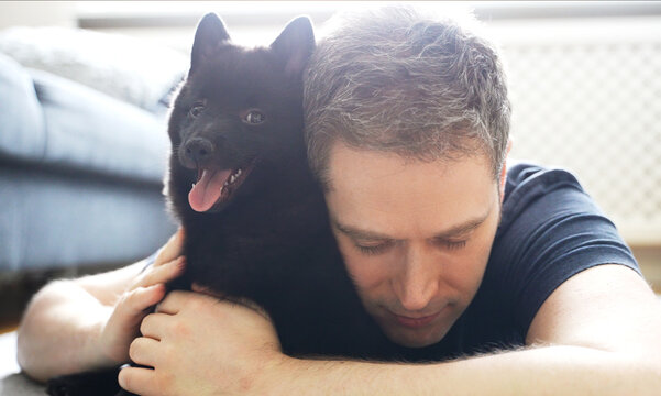 Man hugs his new puppy Schipperke.