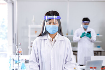 A female scientist looks into a camera and puts on a double face mask. One layer of a mask is inside the science lab..