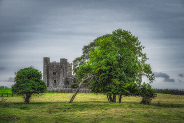 Ruins of old Bective Abbey from 12th century with green trees, pasture and moody dark sky in the background, County Meath, Ireland