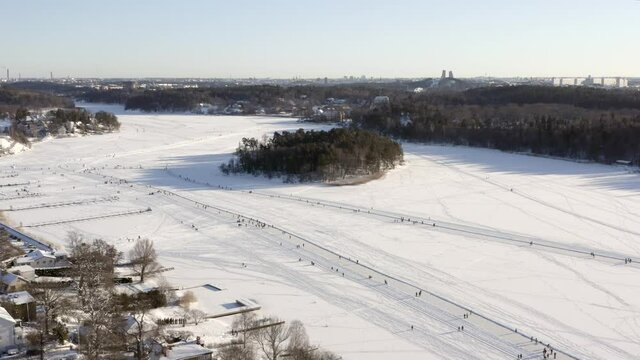 Stockholm winter suburb people ice skating on frozen lake or sea. Aerial shot over ring and nature. leisure family activity in the nature on cold day in white season. City center at horizon in Sweden