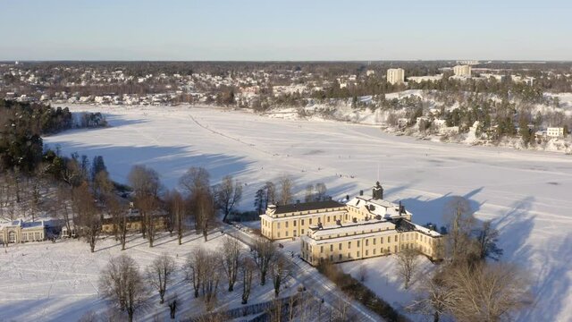 Winter castle palace in snow landscape. Froze ice lake or river with people ice skating. Stockholm Sweden suburb Ulriksdal in aerial drone shot on cold sunny afternoon