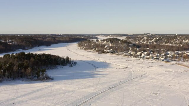Aerial drone view of lake ice surface frozen river with curvy skating paths and skaters on them gliding. White winter landscape in natural nature environment landscape