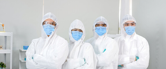 A lab of 4 scientists pretending to be happy inside a ppe suit with protective equipment, a doctor mask and a white ppe suit..