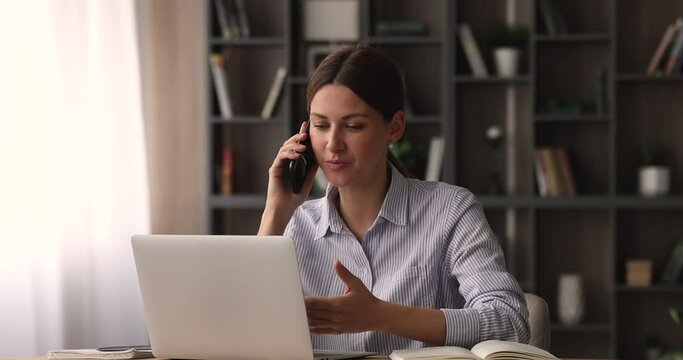 Happy young 35s businesswoman holding smartphone call conversation, discussing online project or brainstorming problem solution with colleagues, working on computer in modern office, multitask concept
