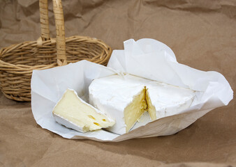 Brie cheese on vintage parchment. Camembert cheese with wooden basket next to it. Italian, French cheese.