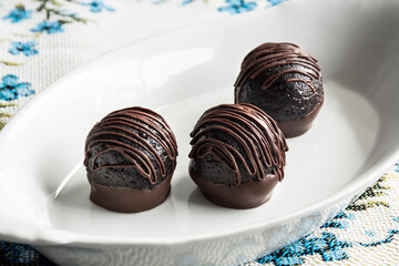 Chocolate truffles in white plate on light background table. Homemade dark chocolate truffles.