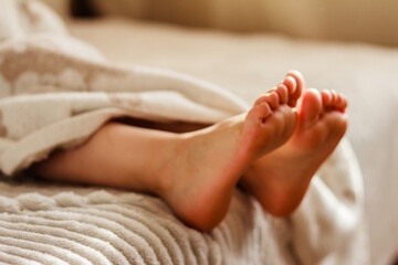 Children`s feet and legs sticking out of soft towel on the bed at home