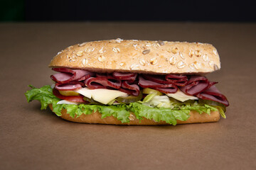 Delicious fresh baguette sandwich with baked ham, cucumber, cheese and salad on ocher background