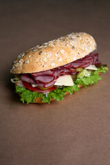 Delicious fresh baguette sandwich with baked ham, cucumber, cheese and salad on ocher background