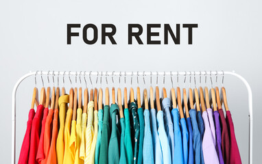 Rack with bright clothes for rent on light background