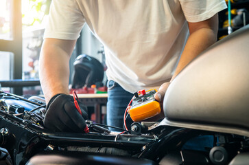 mechanic using multimeter to check the voltage level on motorcycle battery at motorcycle garage,...