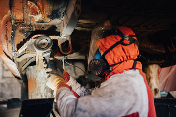 car body work, the master cleans the bottom of the truck with a grinder