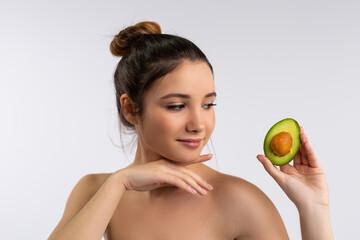 Obraz na płótnie Canvas Portrait of tender young caucasian woman holding a slice of avocado, recommend healthy lifestyle or diet, Smiling female prefer natural organic product for healthy skin teeth, skincare concept