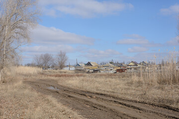 Outskirts of village in early spring. Dirty road, beautiful sky and houses. Rural landscape